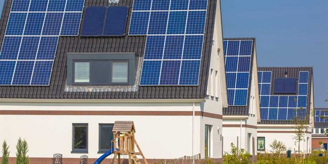 Na imagem, quatro residências equipadas com painéis solares. Na primeira casa, mostrada mais à frente, um pequeno playground para crianças se faz presente.