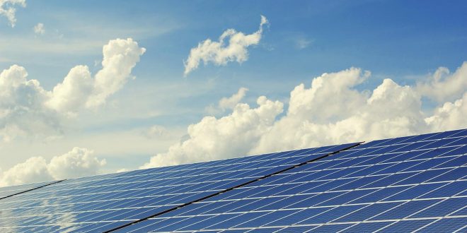 Fotografia mostra painel solar fotovoltaico com céu com nuvens ao fundo.